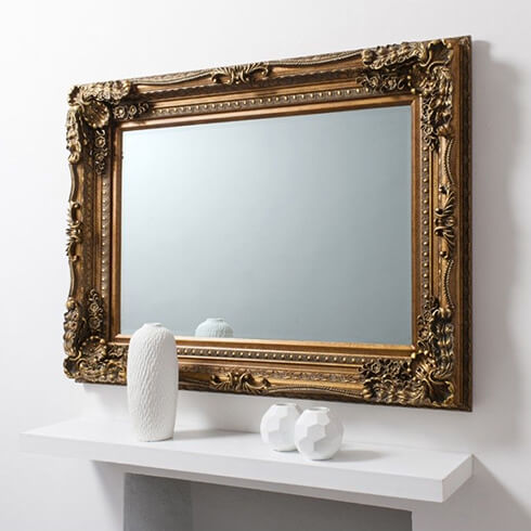 carved swepted framed rectangular gold mirror on wall above mantelpiece