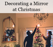 a couple decorating a christmas tree and a gold mirror with christmas decorations