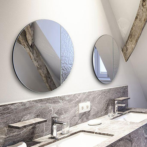 two circular frameless mirrors with textured section hanging above grey marble sink