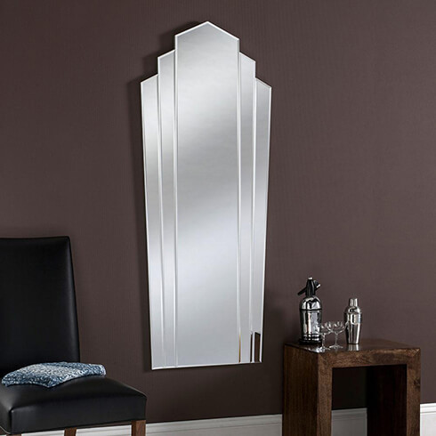fan style frameless art deco bevelled mirror on dark mauve wall with chair and side table