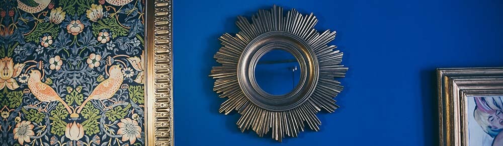 gold sunburst mirror on a blue wall with traditional framed pictures