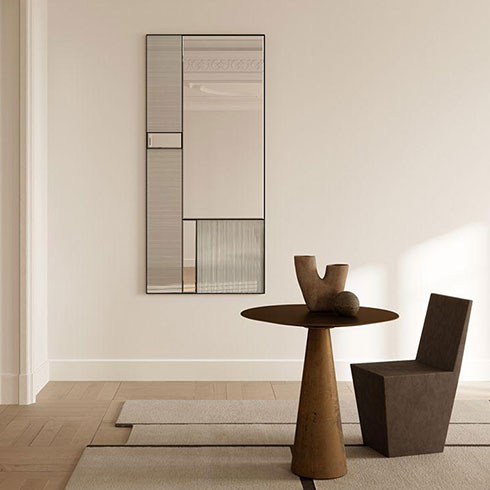 large rectangular wall mirror with panel texture effect and thin black frame hanging on white wall with wooden table and chair
