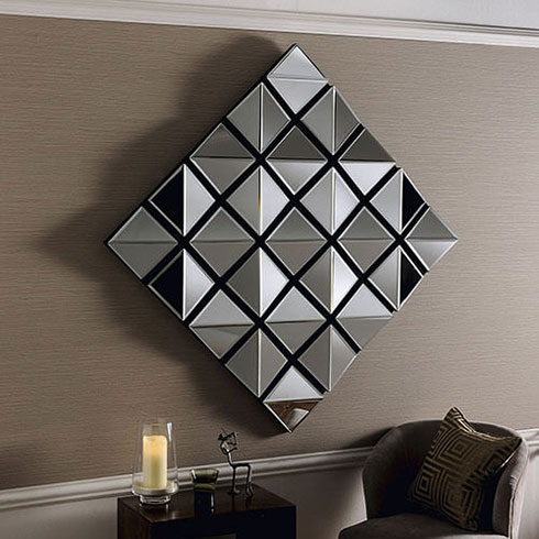 large diamond shaped multi facet frameless bevelled wall mirror hanging on beige wall with chair and table