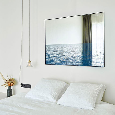large rectangular mirror with seascape print hanging over bed